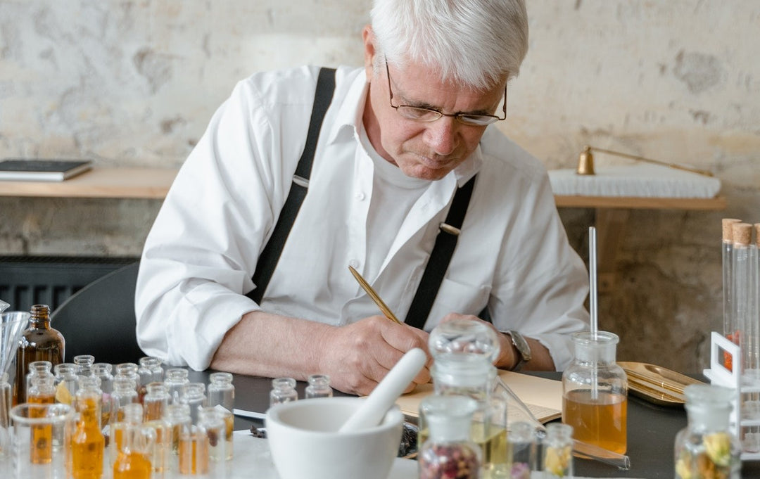 Hombre adulto vestido de blanco con unos tirantes negros elige un perfume fragancia entre una gran variedad